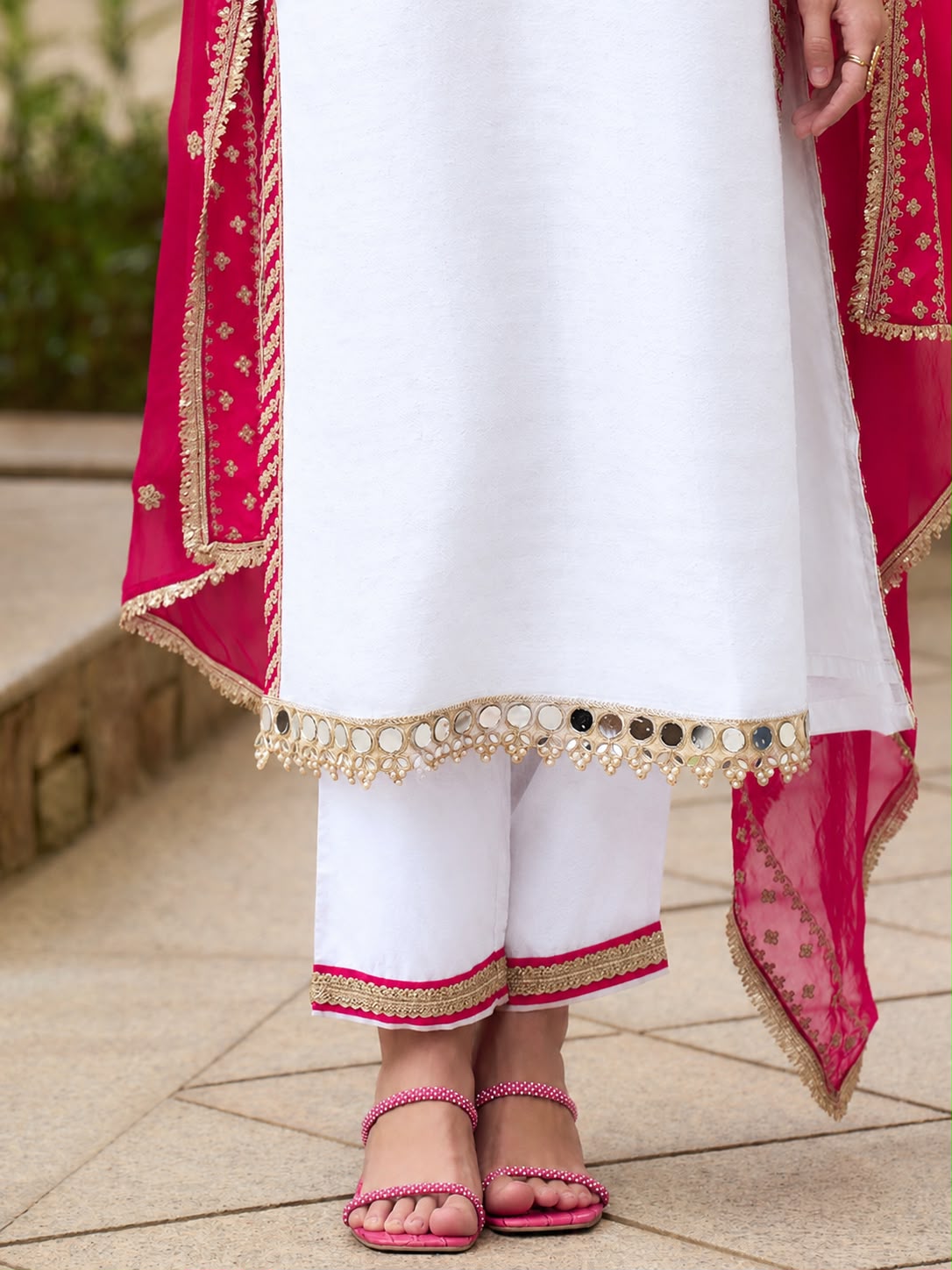 White Hot Pink Chinon Suit Set - close-up portrait garden model showing V-neckline with dense silver zardozi raised petal floral bouquet clusters, gold sequence cascading vine scrollwork, moti pearl bead accents, hot pink bandhani diamond lattice V panel with fine gold zari border, pink silk tassel latkan drops and gold sequence butti hot pink fendy silk dupatta over shoulder