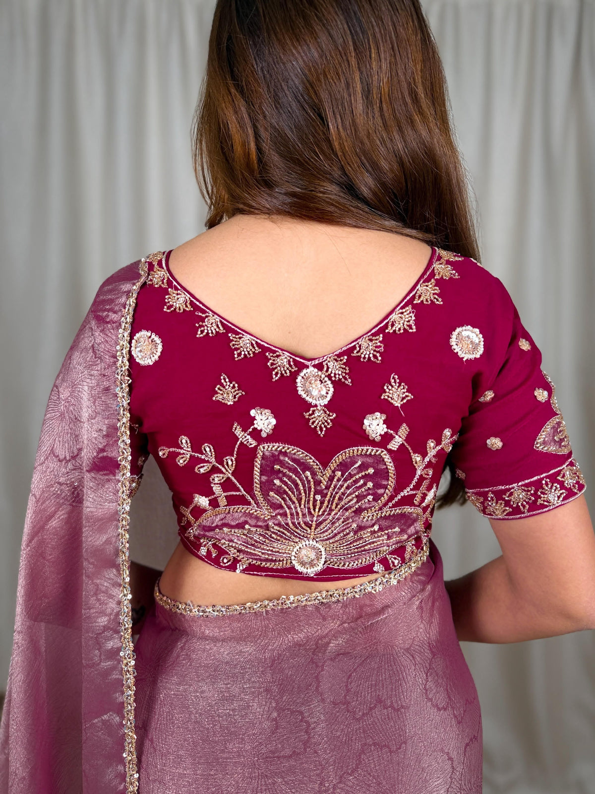 Back styling view of wine red beaded applique blouse with broad V-shaped back neckline, short embellished sleeves and large mauve floral motif, paired with rose mauve saree.