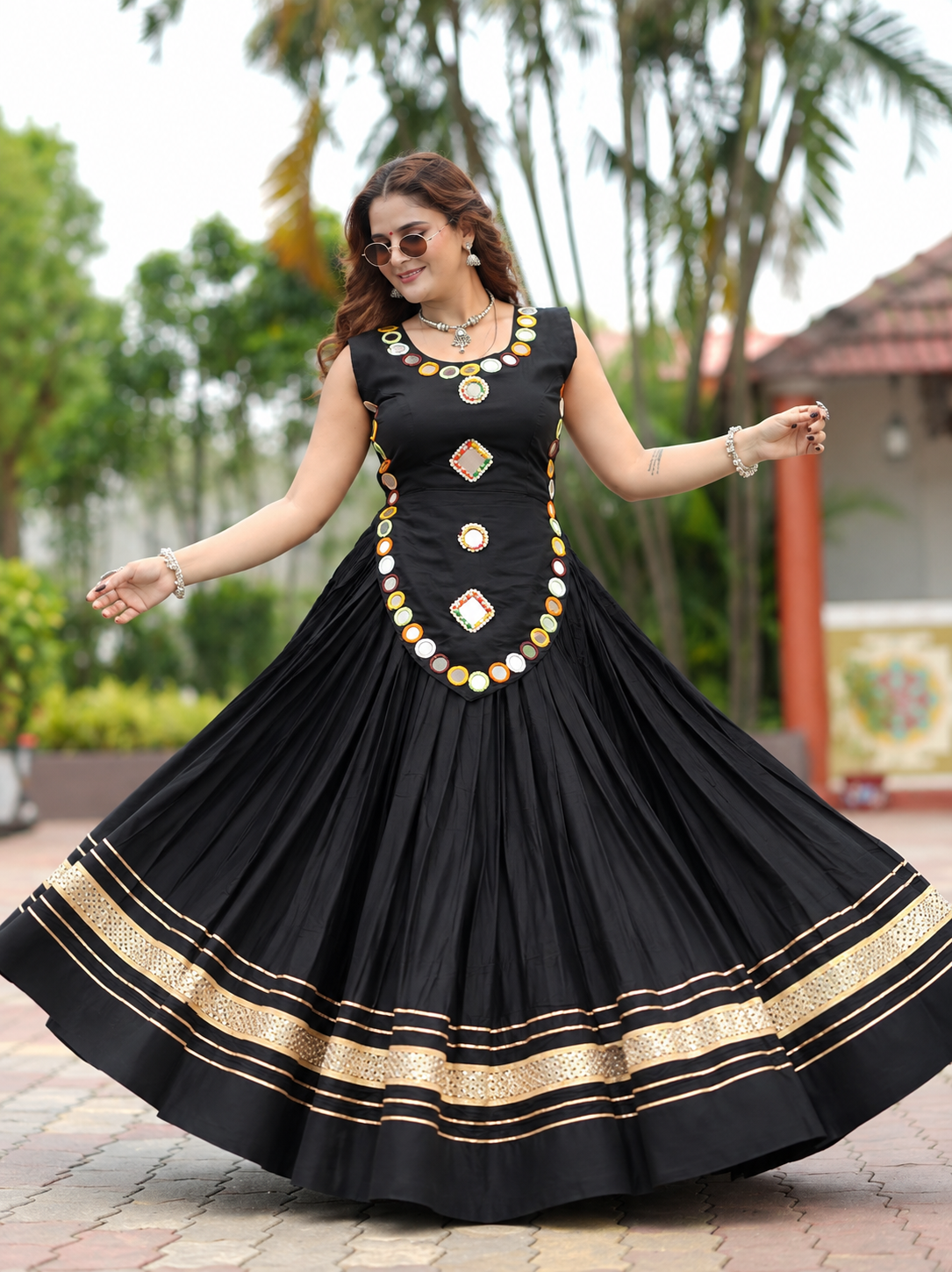 Black Rayon Chaniya Choli Navratri - outdoor garden back view model showing criss-cross lace-up tie back on black blouse with black cord and black tassel drops, and black full-flare lehenga with triple gold zari sequence stripe hem and drawstring black tassel waist tie