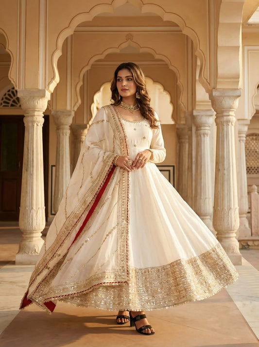 Ivory White Chinon Silk Anarkali Gown Set - palace interior full length twirl view showing complete 52-54 inch gown with all-over coding embroidery and gotta paper sequence work, wide dense gold silver sequence floral daisy hem border, full sleeves with sequence lace cuff, ivory dupatta with gold sequence lace border and red contrast trim edge