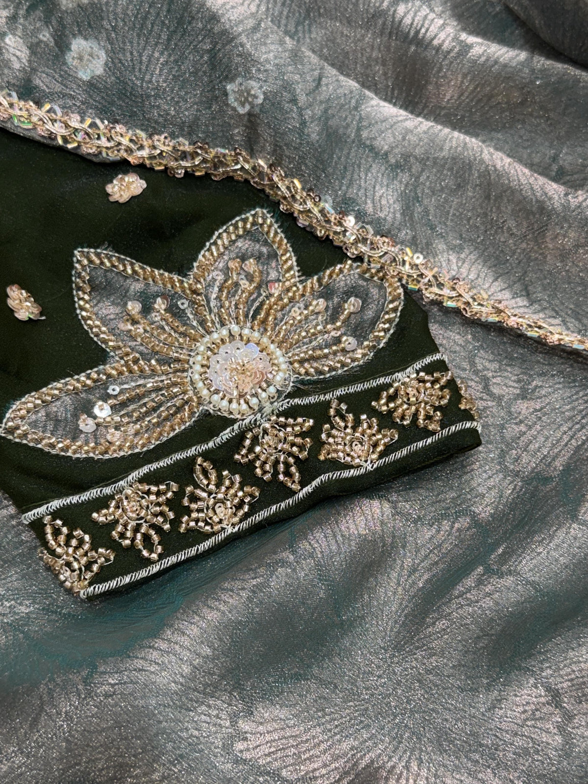 Close-up of silver-grey zari jacquard saree fabric and beads lace edging beside deep green NC moss blouse fabric with floral applique and intricate beads handwork.