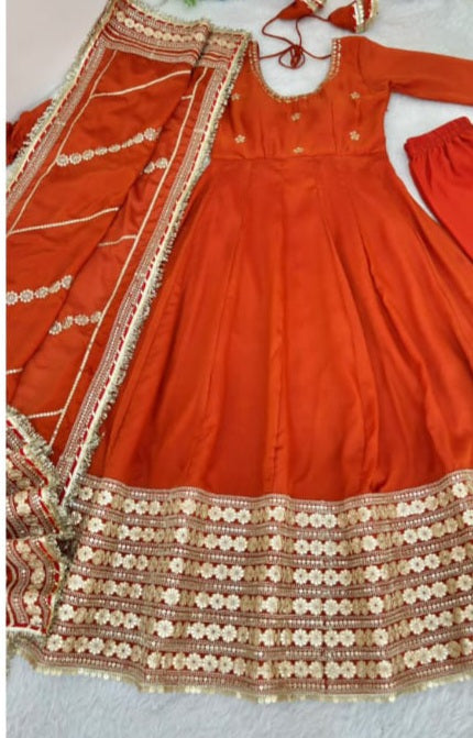 Burnt Orange Rust Chinon Silk Anarkali Gown Set - studio full length standing model view showing complete 52-54 inch Anarkali gown with scattered gold sequence floral butti body, wide scalloped gold sequence floral daisy hem border and matching burnt orange dupatta with multi-stripe gold sequence embroidery