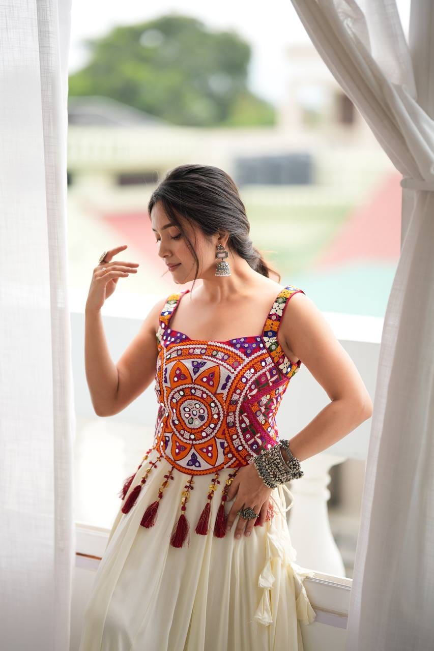 Close-up styling view of multicoloured circular thread embroidery, real mirror detailing, broad straps and maroon latkan tassels on the blouse.