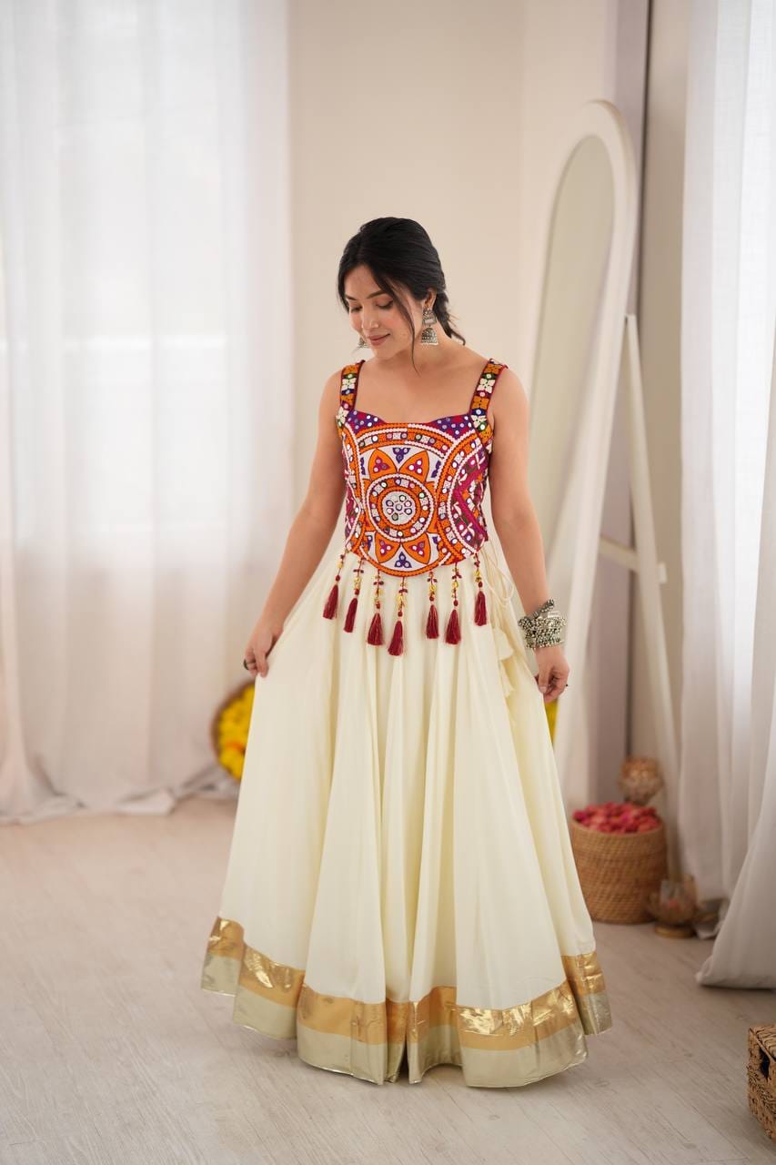 Front styling view of ivory heavy rayon lehenga with gold-tone border and colourful embroidered mirror work blouse with dangling maroon tassels.