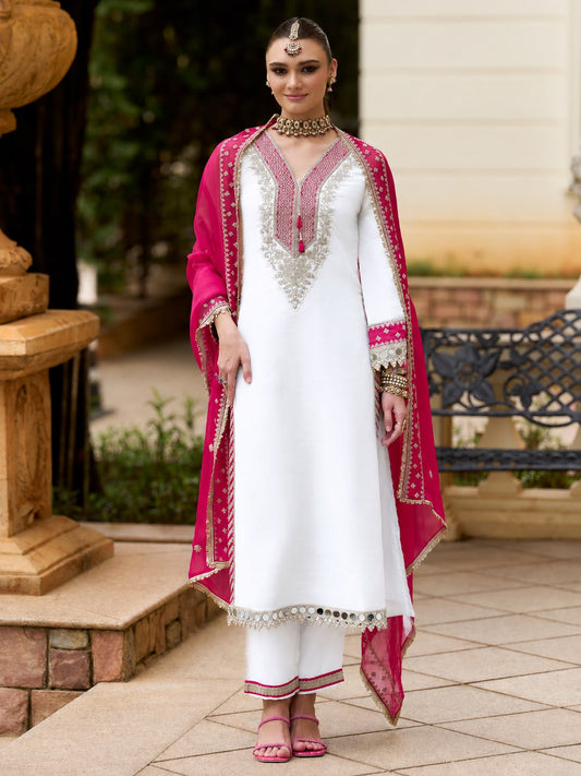 White Hot Pink Chinon Suit Set - outdoor garden half-length portrait model with maang tikka showing complete V-neck with hot pink bandhani yoke, dense silver zardozi gold sequence floral embroidery both sides of V, pink tassel latkan tie and hot pink bandhani sleeve cuffs with real mirror coin lace border
