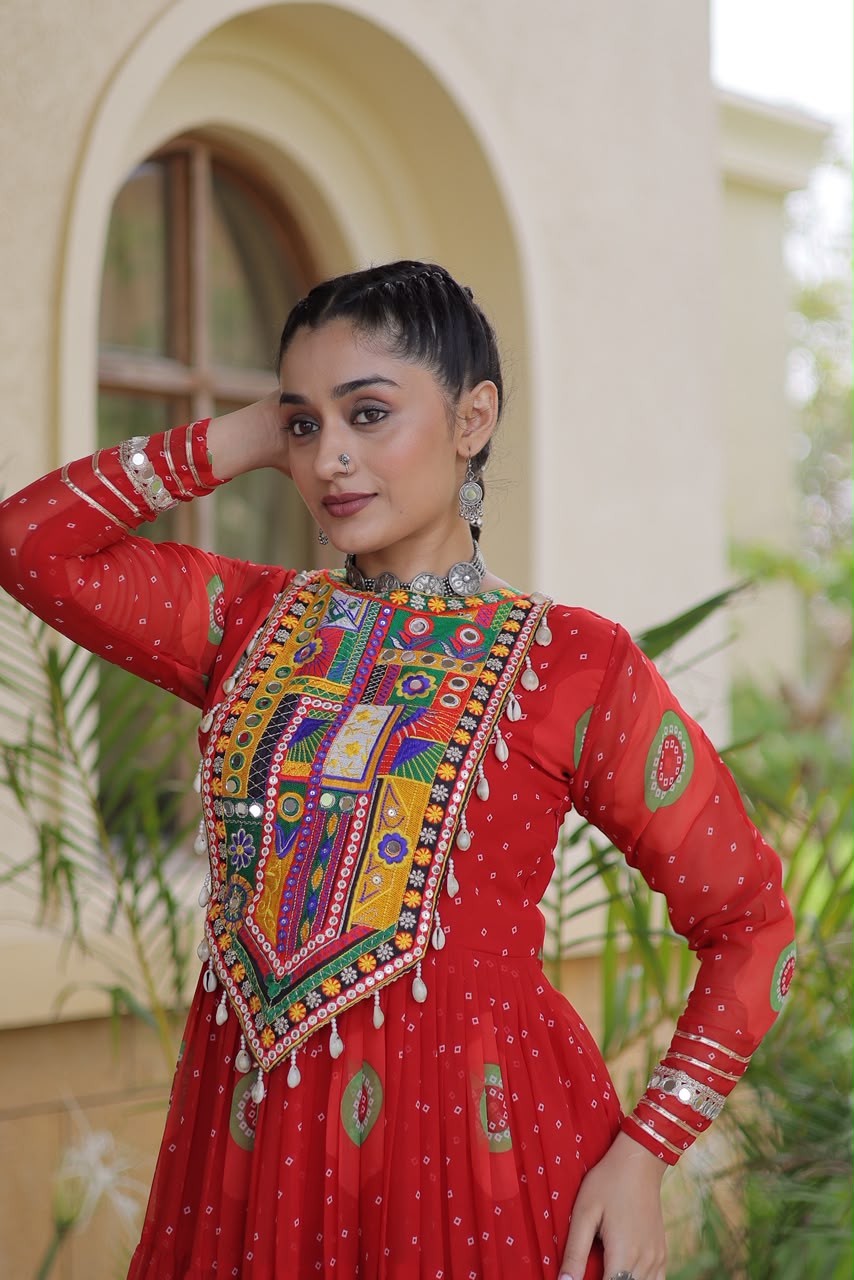 Red Bandhani Faux Georgette Gown - outdoor haveli archway full length front standing view showing complete gown with multicolour Kutchi patchwork yoke, all-over bandhani print with green gold medallions and 12-metre flared silhouette