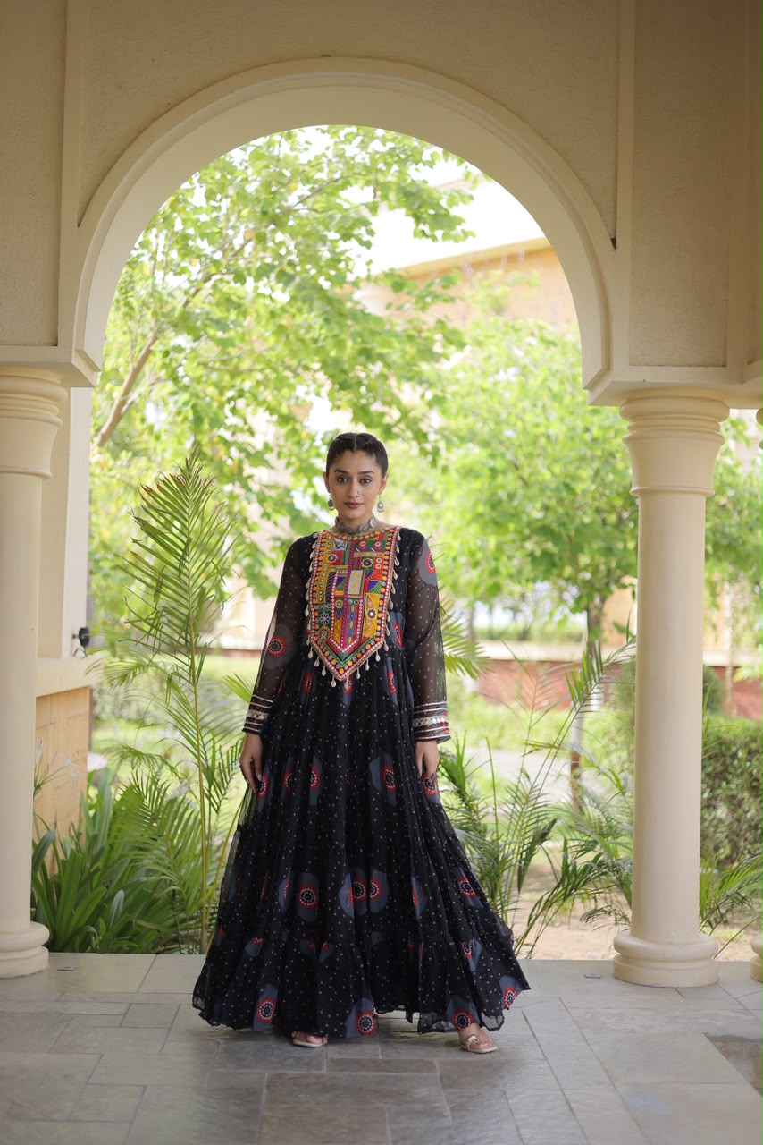 Midnight Black Bandhani Faux Georgette Gown - outdoor haveli archway full length side flowing view showing 12-metre tiered flair with all-over bandhani dot print and pink red teal circular medallion motifs on black ground