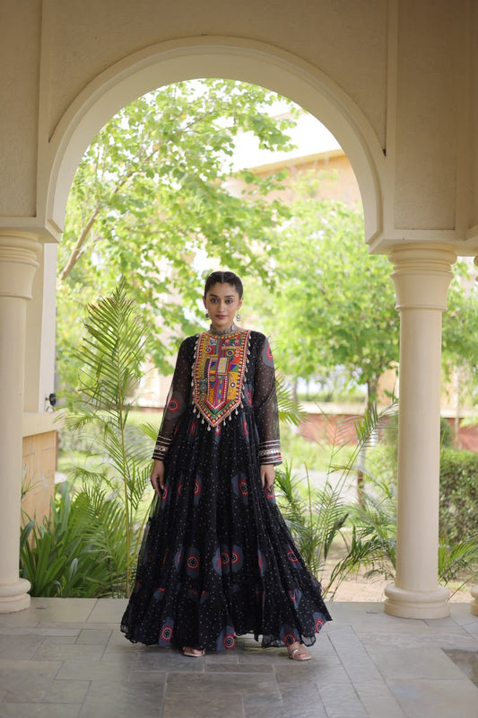 Midnight Black Bandhani Faux Georgette Gown - outdoor haveli archway full length side flowing view showing 12-metre tiered flair with all-over bandhani dot print and pink red teal circular medallion motifs on black ground