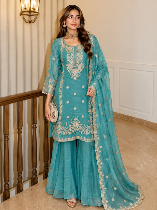 Teal Blue Shalsa Crash Sharara Set - grand interior staircase full length standing model view showing complete 3-piece set with gold zardozi yoke embroidery, scattered sequence circular butti body, scalloped gold sequence floral hem on top and sharara, and matching teal dupatta with dense scattered silver sequence butti and scalloped gold sequence lace border