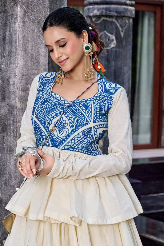 Off-White Royal Blue Kashida Gamthi Lehenga Set - heritage haveli exterior upper body close-up portrait of model showing royal blue Kashida Gamthi geometric bodice panel with square diamond grid lotus floral medallion folk motifs in deep royal blue thread, sweetheart scoop neckline with black rope cord tie necklace, sheer organza full sleeves, and beginning of double-tiered gathered peplum flair