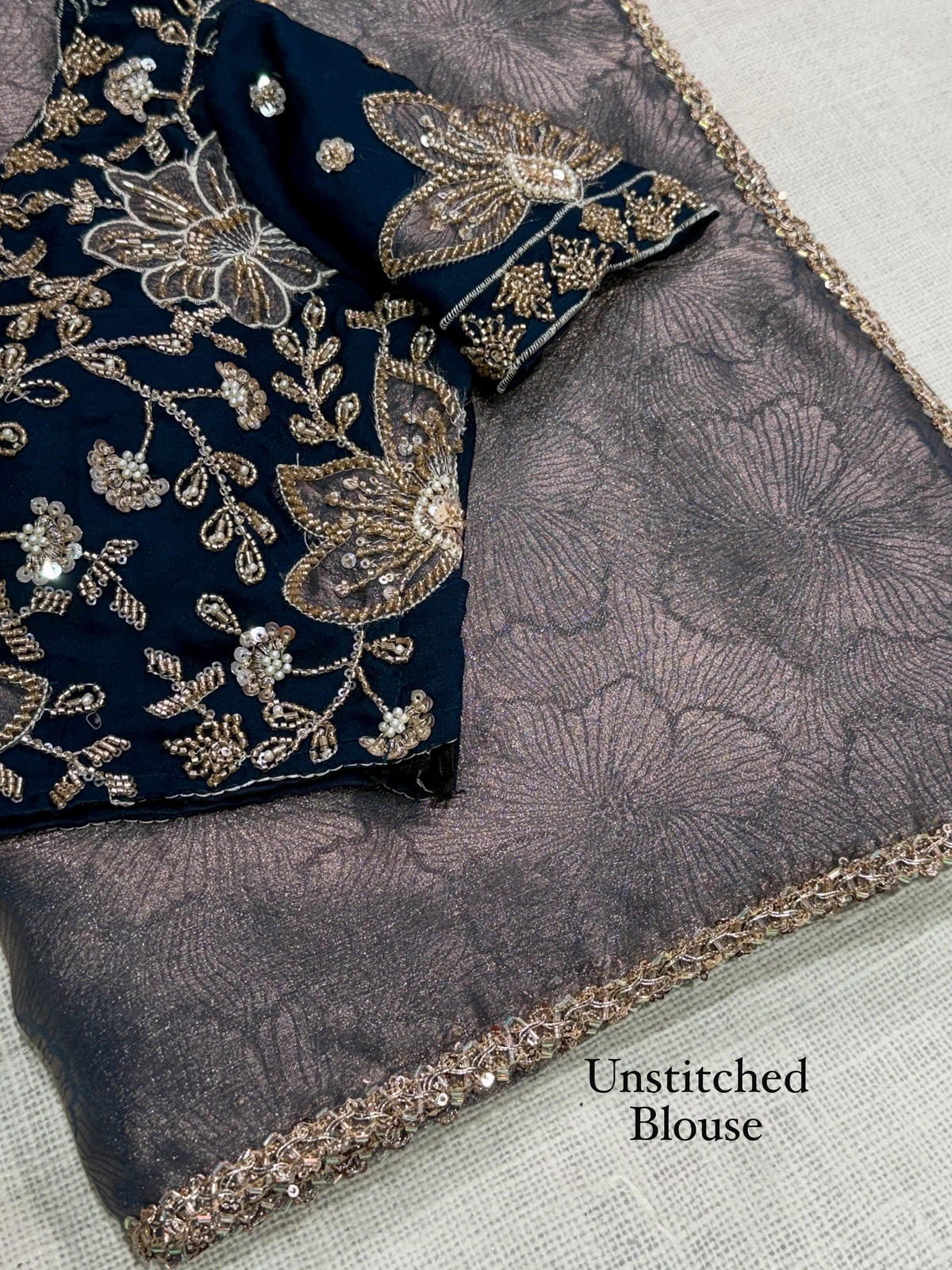 Close-up of slate grey floral jacquard weaving and beads lace border beside navy blue unstitched blouse fabric with beaded floral applique and leafy vines.