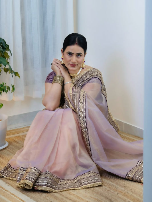 Dusty Mauve Soft Twill Net Saree - indoor bright interior seated model with elaborate gold jewellery set showing complete saree draped with triple-tier gold sequence geometric dori embroidery border at hem clearly visible and deep aubergine jacquard silk blouse