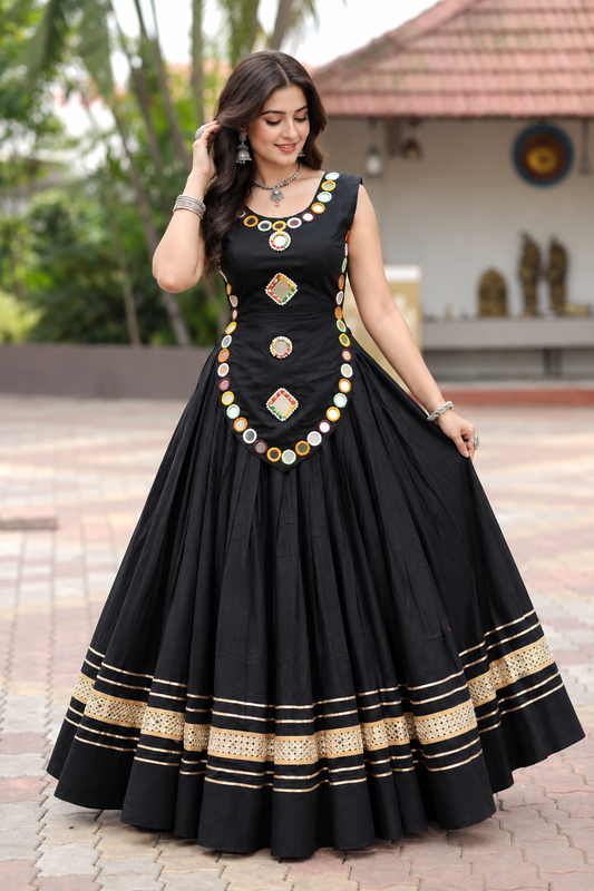 Black Rayon Chaniya Choli Navratri - outdoor garden full length standing model front view showing black sleeveless blouse with real multicolour round mirror neckline, square and round mirror bodice panel, scallop overlay with mirror ring border, and black full-flare lehenga with triple gold zari sequence stripe hem