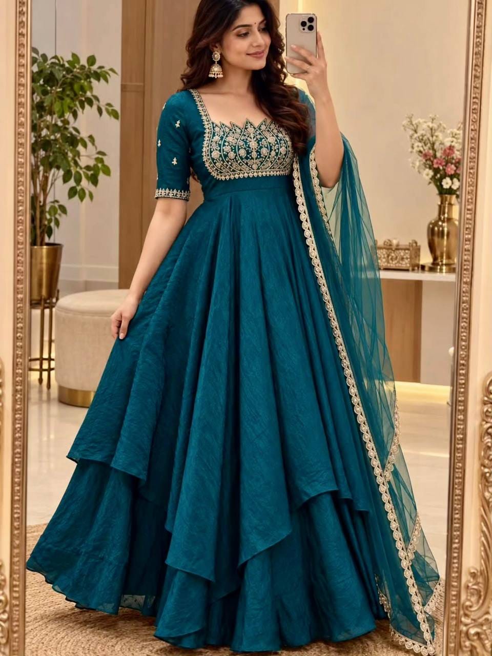 Model styling a teal blue Fandy crush silk lotus Anarkali gown with embellished bodice, elbow-length sleeves, cascading layered skirt and bordered net dupatta.