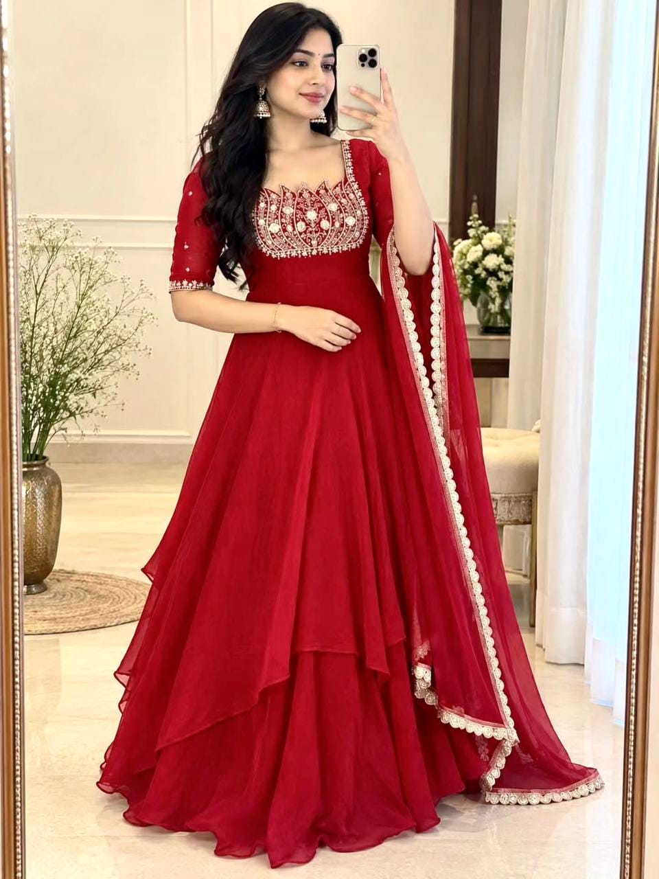 Model styling a crimson red lotus Anarkali gown with embellished bodice, cascading asymmetric skirt layers and sheer red embroidered border dupatta.