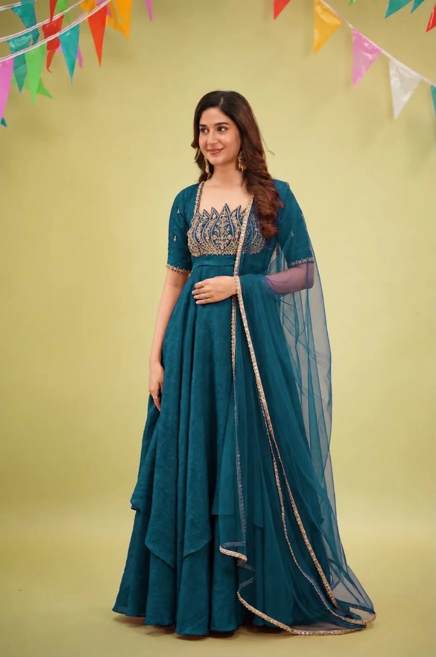 Full-length styling view of teal blue layered Anarkali gown with lotus bodice embroidery and matching sheer dupatta draped over one shoulder.